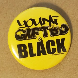 Könnte beinhalten: Gelber Knopf mit schwarzem Text, der "Young Gifted & Black" lautet, mit den Worten "Outspoken Kwanzaa" unten.