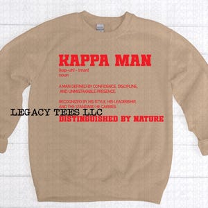 May include: A tan sweatshirt with the words "KAPPA MAN" in red block letters. Below the text is a definition of the term. The sweatshirt also has the text "LEGACY TEES LLC DISTINGUISHED BY NATURE".