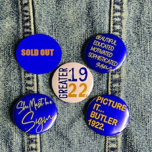 May include: Five blue and gold buttons with different text. The buttons say "Sold Out", "Beautiful Educated Motivated Sophisticated", "Greater 19 22", "She Must be a Sigma", and "Picture It... Butler 1922."