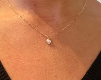 May include: A delicate gold chain necklace with a small round pendant featuring a clear, sparkling stone.