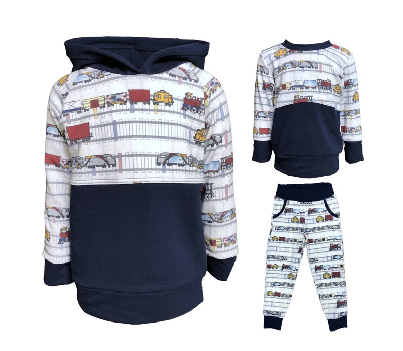 May include: A three-piece toddler boy's clothing set featuring a navy blue hooded sweatshirt, a navy blue long-sleeve shirt, and navy blue sweatpants. All pieces feature a white background with a repeating pattern of colorful trains and railroad tracks.