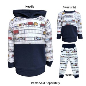 May include: A set of children's clothing featuring a navy blue hoodie, sweatshirt, and joggers with a white and blue train pattern. The text "Hoodie", "Sweatshirt", and "Joggers" are printed on the image. The text "Items Sold Separately" is printed at the bottom of the image.