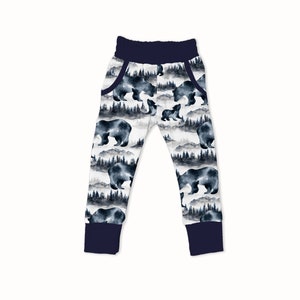 May include: White sweatpants with a navy blue waistband and cuffs. The sweatpants have a watercolor print of bears and trees in shades of blue and gray.