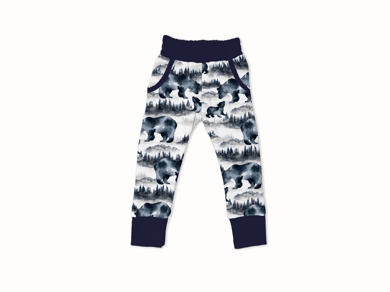 May include: White sweatpants with a navy blue waistband and cuffs. The sweatpants have a watercolor print of bears and trees in shades of blue and gray.