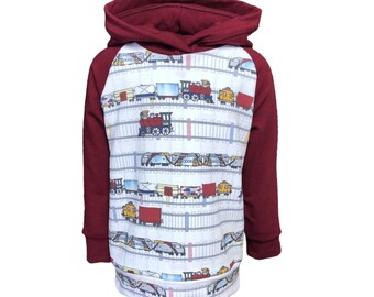 May include: A white hooded sweatshirt with a red raglan sleeve design. The front of the sweatshirt features a repeating pattern of colorful toy trains on a white background.