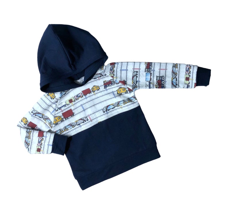 May include: A navy blue hooded sweatshirt with a white and blue train pattern on the top half. The bottom half of the sweatshirt is solid navy blue.