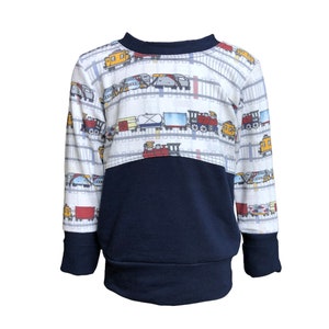 May include: A white long-sleeved sweatshirt with a navy blue bottom half. The top half features a repeating pattern of colorful trains on white railroad tracks.