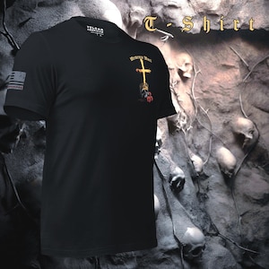 Pu&ograve; includere: T-shirt nera con la scritta "T-Shirt" in oro. La maglietta presenta un disegno a croce dorata con le parole "Memento Mori" e una piccola bandiera americana sulla manica. La maglietta &egrave; realizzata in materiale morbido.