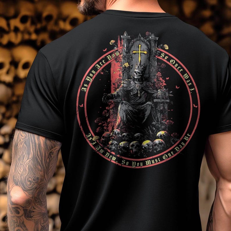Pu&ograve; includere: T-shirt nera con una grafica circolare di un re scheletro su un trono, con una croce e la scritta "As You Are Now, So You Must One Day Be". Il design include teschi e rose.