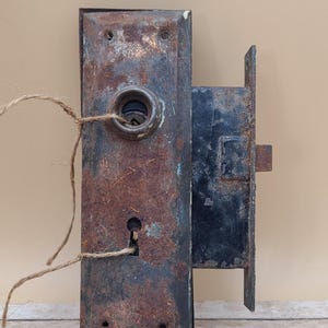 May include: A rusty metal door lock with a keyhole and a round knob. The lock is attached to a wooden door frame.