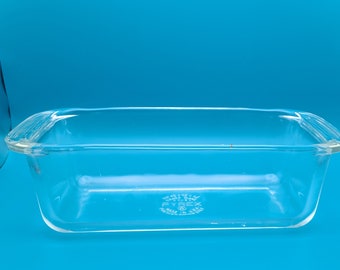 May include: A clear glass loaf pan with a Pyrex logo on the bottom. The pan is empty and sitting on a blue surface.