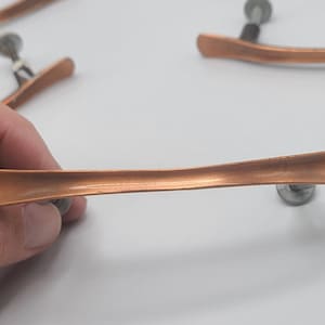 May include: A set of five copper cabinet door pulls with a curved design and silver screws.