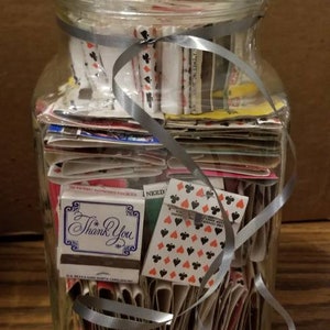 May include: A glass jar filled with a stack of playing cards and matchbooks. The jar is tied with a silver ribbon and has a clear lid. The matchbooks have a "Thank You" message on the front.