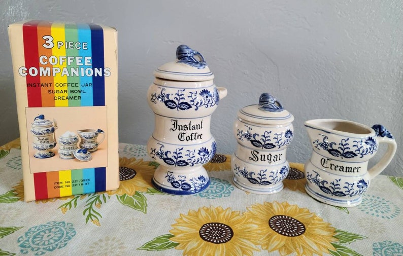 K&ouml;nnte beinhalten: Ein Set aus drei blauen und wei&szlig;en Keramik-Kaffeebegleitern. Das Set enth&auml;lt einen Milchk&auml;nnchen, eine Zuckerdose und ein Glas f&uuml;r Instantkaffee. Jedes St&uuml;ck ist mit einem Blumendesign verziert und tr&auml;gt den Schriftzug "Sahne", "Zucker" oder "Instantkaffee" auf der Vorderseite.