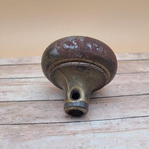 May include: A vintage brass door knob with a worn, rusty finish. The knob has a round, domed top and a cylindrical base with a hole in the center.