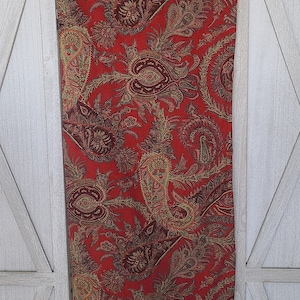 May include: Red paisley patterned fabric with a gold and brown design. The fabric is hanging on a white wooden door.