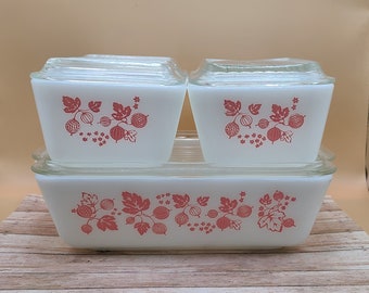 May include: A set of three white glass storage containers with pink and white gooseberry designs. The containers are stacked on top of each other.