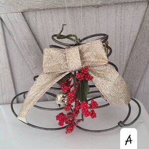 May include: A gold glitter ribbon bow is tied around a metal wire Christmas tree. The tree is decorated with red berries and a silver bell.