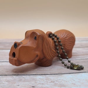 May include: A brown ceramic dog keychain with a gold chain. The dog has a long snout and floppy ears.