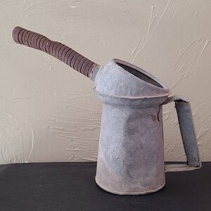 May include: A vintage metal oil can with a brown, ribbed spout and a handle. The can is weathered and has a gray finish.