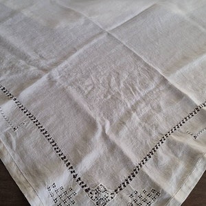 May include: White linen tablecloth with delicate embroidered lace trim. The tablecloth has a square shape and is made of a soft, natural fabric.