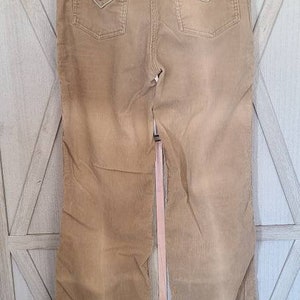 May include: A pair of light brown corduroy pants with a wide leg and a slight flare at the bottom. The pants have two pockets on the back and a small brand label on the right pocket.