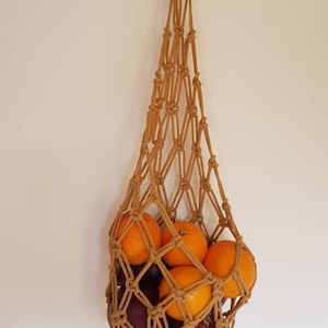 May include: A brown macrame hanging basket filled with oranges and purple onions.