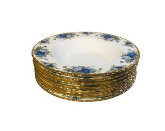 May include: A stack of 10 white ceramic soup bowls with a blue and gold floral pattern. The bowls have a gold rim and are stacked on top of each other.