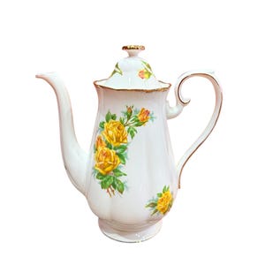 Könnte beinhalten: Weiße Porzellan-Teekanne mit goldener Verzierung und einem Blumendesign mit gelben Rosen. Die Teekanne hat einen Deckel und einen Henkel.