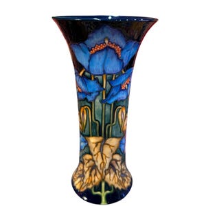 Puede incluir: Un jarrón de cerámica azul y blanco con un diseño floral. El jarrón es alto y delgado con una parte superior acampanada. Las flores son azules con centros amarillos y hojas verdes.