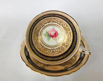May include: A vintage teacup and saucer set with a delicate floral design. The cup and saucer are decorated with gold trim and a blue band.