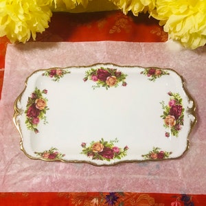 May include: A white rectangular serving tray with a gold rim and a floral design featuring red, pink, and yellow roses. The tray has a scalloped edge.
