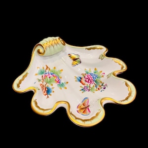 May include: A white porcelain serving dish shaped like a seashell with a green and gold rim. The dish is decorated with colorful flowers and butterflies.