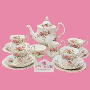 Peut inclure: Un service à thé en porcelaine blanche orné d'un motif floral de roses roses avec des feuilles vertes et un liseré doré. Il comprend une théière, un pot à lait, un sucrier et quatre tasses avec soucoupes. Une plaque indique ROYAL ALBERT MADE IN ENGLAND.