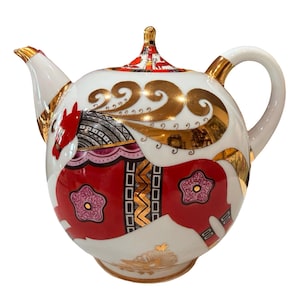May include: A white porcelain teapot featuring a stylised red horse motif with gold accents. The design includes intricate geometric patterns, floral shapes, and a gold-trimmed handle, spout, and lid. The horse is depicted in profile with a red body.