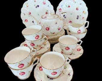 Può includere: Un servizio da tè vintage completo con teiera, tazze, piattini, piatti e una lattiera. Il set in porcellana bianca è decorato con un motivo di mele rosse, bacche viola e foglie verdi, con bordi dorati.