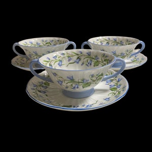 May include: Three white porcelain soup bowls with blue floral designs and blue trim. Each bowl has two handles and comes with a matching saucer.