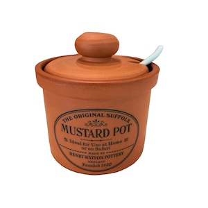 May include: A terracotta-colored mustard pot with a lid and a small spoon. The pot has a rounded shape with a label that reads "The Original Suffolk Mustard Pot." The label also includes the text "Made by Henry Watson Pottery England Founded 1800."