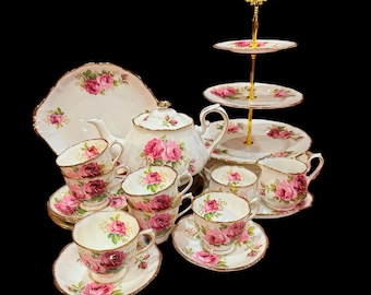 Peut inclure: Service à thé vintage complet, comprenant une théière, des tasses, des soucoupes, une assiette de service et un présentoir à étages. La porcelaine blanche est ornée de motifs floraux de roses roses et de bordures dorées.