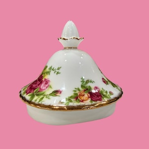Peut inclure: Couvercle en porcelaine blanche avec une bordure dorée et un motif floral de roses rouges, roses et jaunes. Le couvercle a un bouton conique, probablement pour un récipient décoratif.