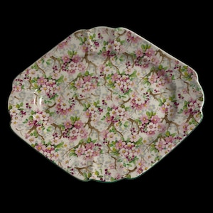 May include: A white ceramic serving platter with a green rim and a floral pattern of pink and green flowers on a white background.