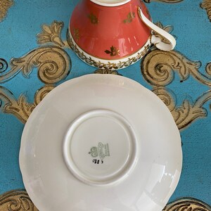 May include: A white teacup and saucer with a gold rim and floral design. The saucer has a scalloped edge. The teacup and saucer are marked with the Aynsley England Bone China logo.