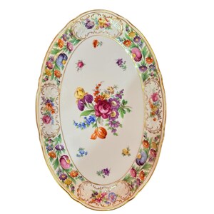 May include: Oval porcelain serving platter with a floral design. The white platter features a gold trim and a border of colorful flowers. A central bouquet of red, purple, yellow, and blue flowers decorates the center of the platter.