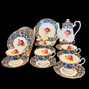 May include: A black and white tea set with a delicate floral design. The set includes a teapot, creamer, sugar bowl, six teacups, and six saucers. The teacups and saucers have a black lace pattern with a pink rose design.