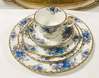 May include: A set of four white porcelain teacups and saucers with a blue and gold floral pattern. The cups and saucers have a delicate, scalloped edge.