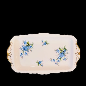 Peut inclure: Un plateau de service rectangulaire blanc avec un bord doré et un motif floral composé de fleurs bleues et vertes de myosotis.