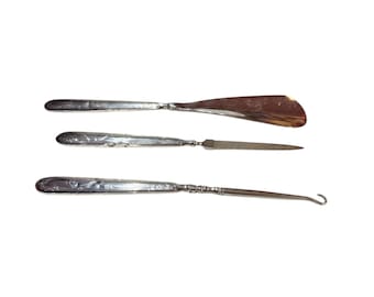 May include: A set of three silver shoe horns. The shoe horns are all the same length and have a decorative design on the handle. The shoe horns are used to help put on shoes.