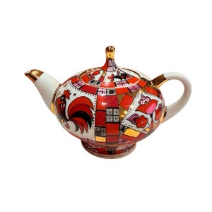 Peut inclure: Une théière en porcelaine ornée d'un motif géométrique vibrant dans des tons de rouge, orange et noir, rehaussée de bordures dorées. Le design comprend une illustration de coq stylisé et des motifs floraux, avec un couvercle assorti.