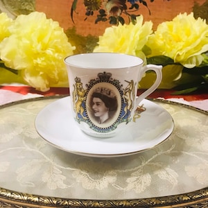 Op de afbeelding: Een wit theekopje en schotel met een gouden rand. Het kopje heeft een portret van koningin Elizabeth II en de tekst "June 2nd 1953 Coronation".