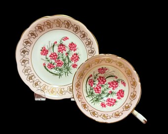 May include: A vintage teacup and saucer set. The set features a pink and white floral design with gold trim. The teacup has a handle and the saucer is round. The floral design includes pink flowers and green leaves.